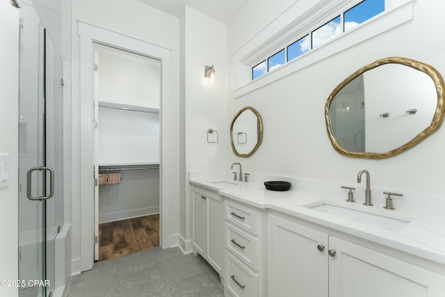 full bathroom with double vanity, a spacious closet, a shower stall, and a sink