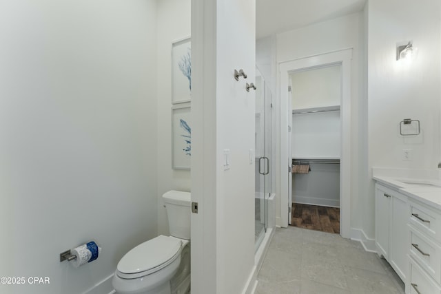 full bath with a shower stall, toilet, vanity, baseboards, and a spacious closet