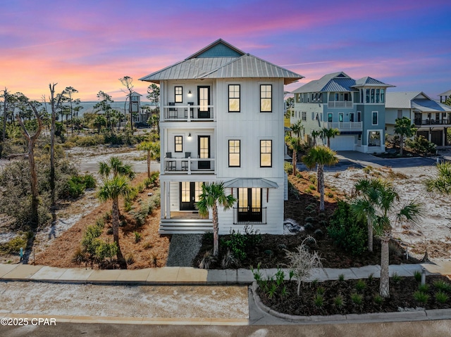 raised beach house featuring a standing seam roof, metal roof, driveway, a balcony, and an attached garage