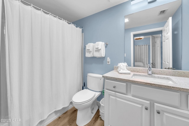 bathroom with toilet, vanity, wood finished floors, and visible vents
