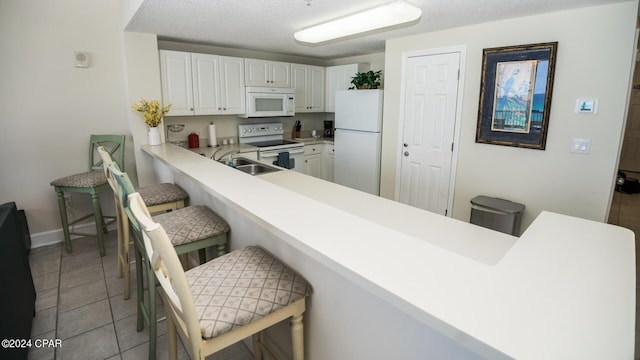 kitchen with white appliances, light countertops, a kitchen bar, white cabinetry, and light tile patterned floors