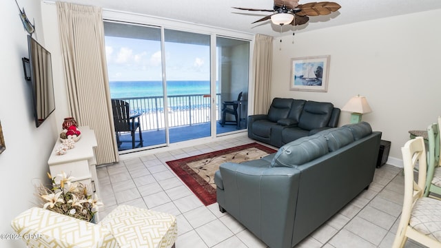 living area with ceiling fan, a water view, light tile patterned floors, and expansive windows