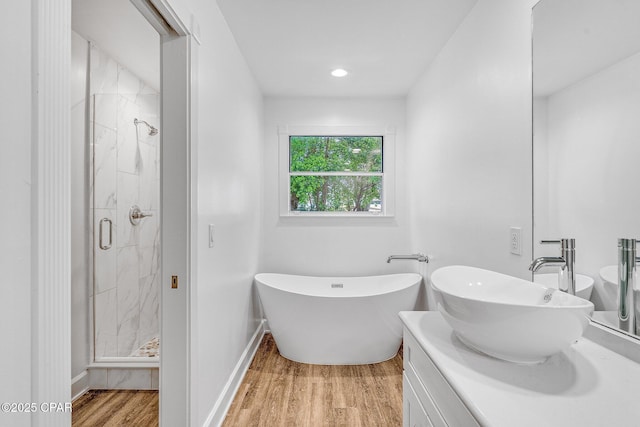 bathroom featuring wood finished floors, a freestanding bath, vanity, baseboards, and a marble finish shower