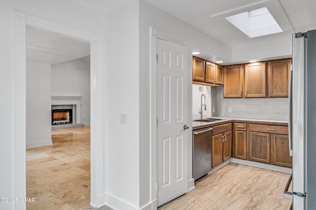 kitchen with a skylight, brown cabinetry, appliances with stainless steel finishes, backsplash, and a sink