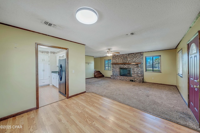 unfurnished living room with a textured ceiling, visible vents, ceiling fan, and a fireplace