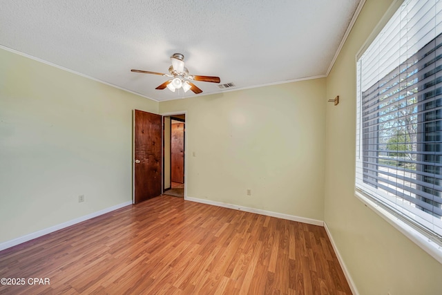 spare room featuring a textured ceiling, light wood finished floors, baseboards, ceiling fan, and ornamental molding
