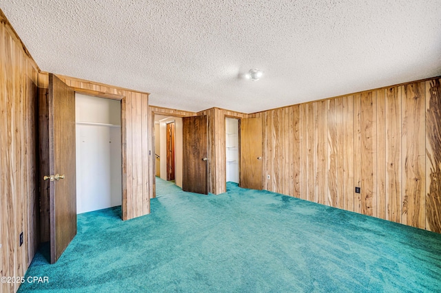 unfurnished bedroom featuring carpet flooring, wood walls, and a textured ceiling