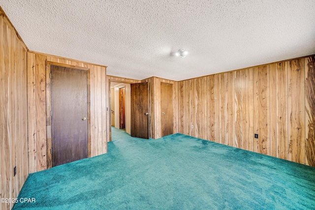 unfurnished bedroom with carpet floors, a textured ceiling, and wooden walls