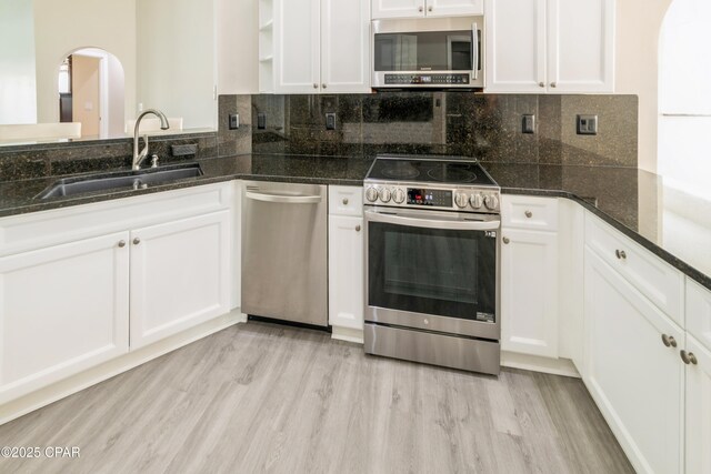 kitchen featuring arched walkways, light wood-type flooring, white cabinets, appliances with stainless steel finishes, and a sink