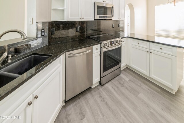 kitchen featuring a peninsula, light wood-style floors, stainless steel appliances, arched walkways, and a sink