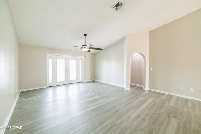 spare room with light wood-type flooring, baseboards, visible vents, ceiling fan, and arched walkways