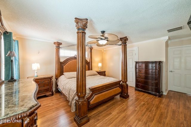 bedroom featuring ornamental molding, visible vents, light wood-type flooring, and a textured ceiling