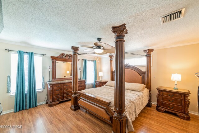 bedroom with ornamental molding, visible vents, decorative columns, and light wood-style floors