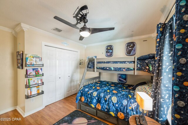 bedroom with baseboards, a closet, ornamental molding, visible vents, and wood finished floors