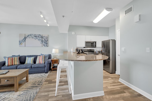 kitchen with white cabinetry, a kitchen bar, stainless steel appliances, decorative backsplash, and visible vents