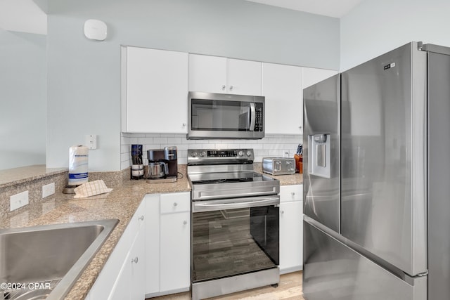 kitchen featuring light stone countertops, appliances with stainless steel finishes, white cabinetry, a sink, and backsplash