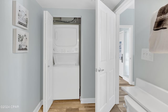 laundry room featuring baseboards, light wood-style flooring, stacked washer / dryer, and laundry area