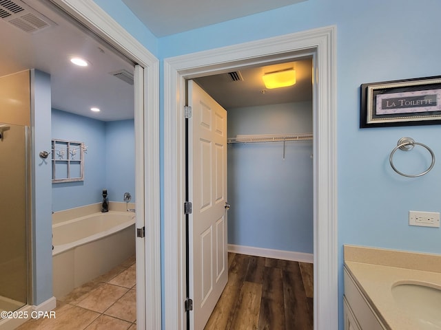 bathroom with a garden tub, a shower stall, a spacious closet, vanity, and recessed lighting