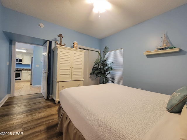 bedroom featuring wood finished floors, freestanding refrigerator, a closet, baseboards, and ceiling fan