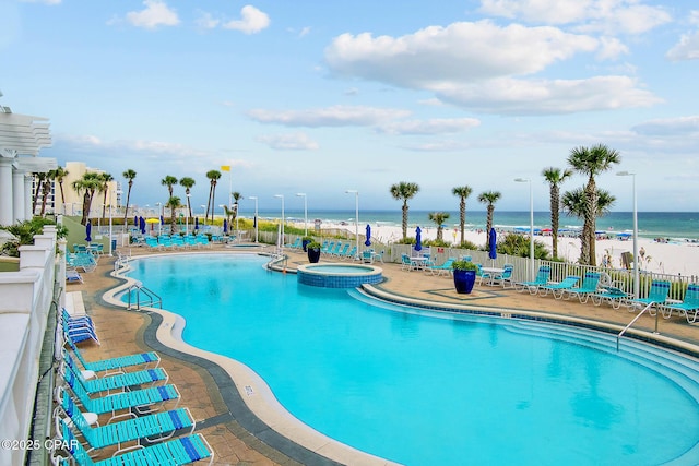 view of swimming pool with view of water and beach, fence, a patio area, and a pool with connected hot tub