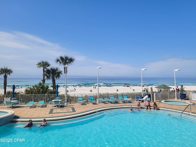 community pool with a community hot tub, a water view, a patio area, and fence