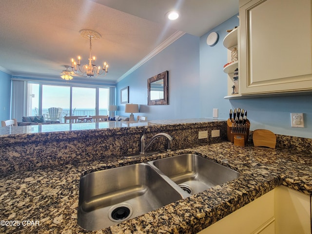 kitchen with a sink, crown molding, a chandelier, open floor plan, and dark stone counters