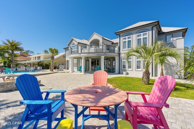 4522 Bay Point Rd, Panama City Beach, FL 32408 - rear view of house featuring a standing seam roof, metal roof, a balcony, outdoor dining space, and a patio area