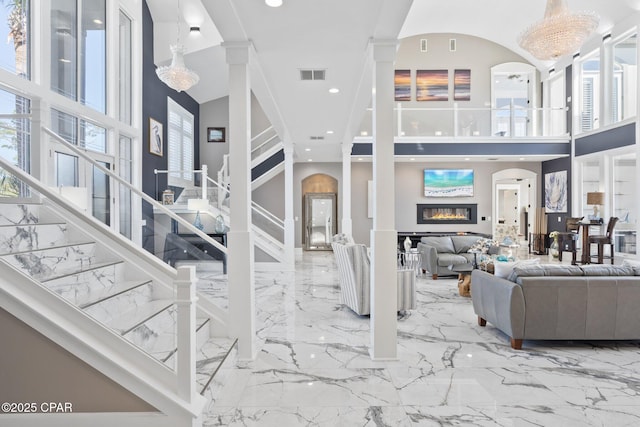 4522 Bay Point Rd, Panama City Beach, FL 32408 - living area with visible vents, marble finish floor, a glass covered fireplace, stairway, and a high ceiling