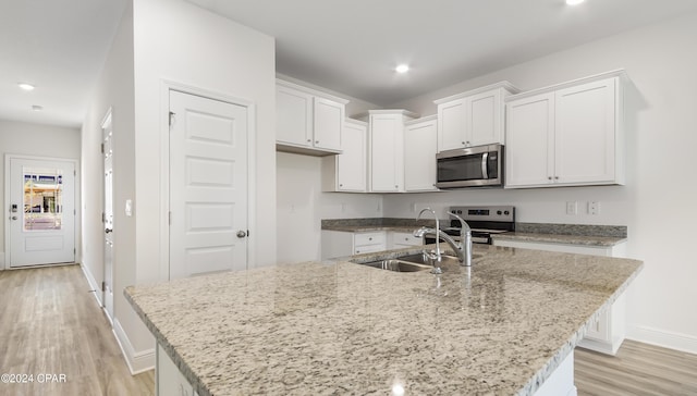 kitchen featuring appliances with stainless steel finishes, a center island with sink, a sink, white cabinets, and light wood-style flooring