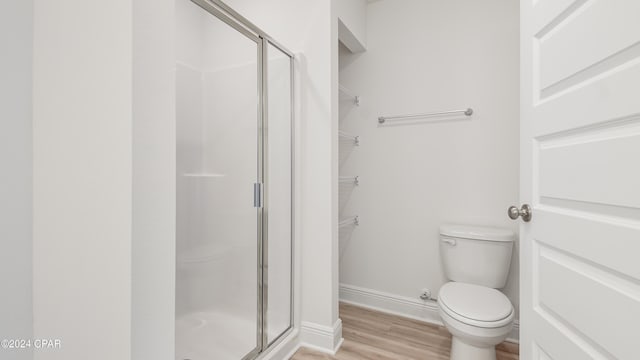 bathroom featuring a stall shower, toilet, wood finished floors, and a spacious closet