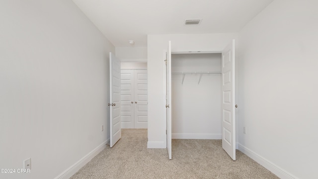 unfurnished bedroom with light colored carpet, baseboards, visible vents, and a closet