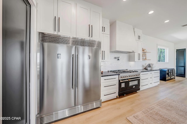 7603 Coastal Hammock Trl, Panama City Beach, FL 32413 - kitchen with high end appliances, wall chimney range hood, light wood-style flooring, tasteful backsplash, and white cabinets