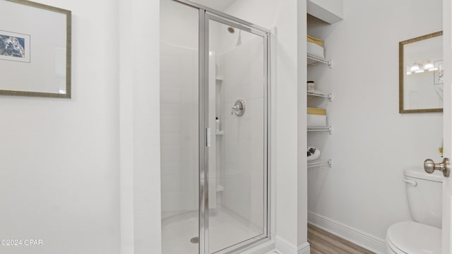 bathroom featuring toilet, wood finished floors, baseboards, and a stall shower