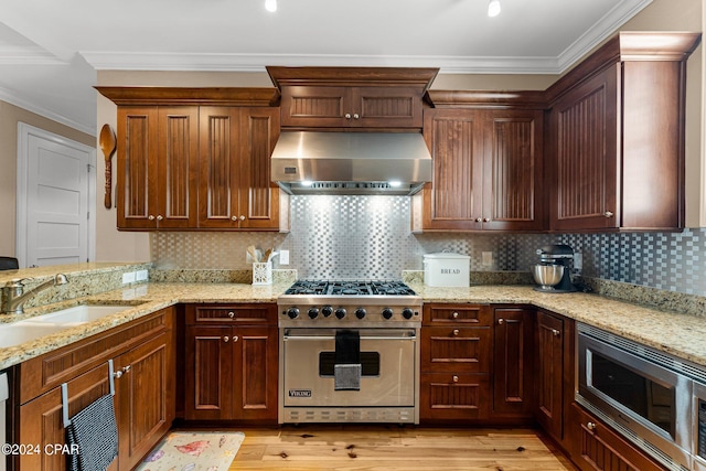 kitchen featuring wall chimney range hood, stainless steel appliances, light wood-type flooring, and a sink