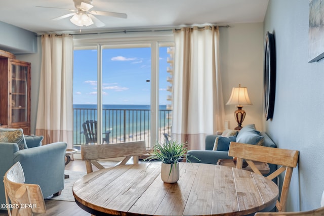 dining area with a ceiling fan, a water view, and wood finished floors