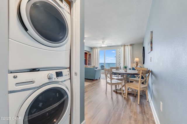 clothes washing area with a textured ceiling, stacked washer and clothes dryer, baseboards, wood finished floors, and laundry area