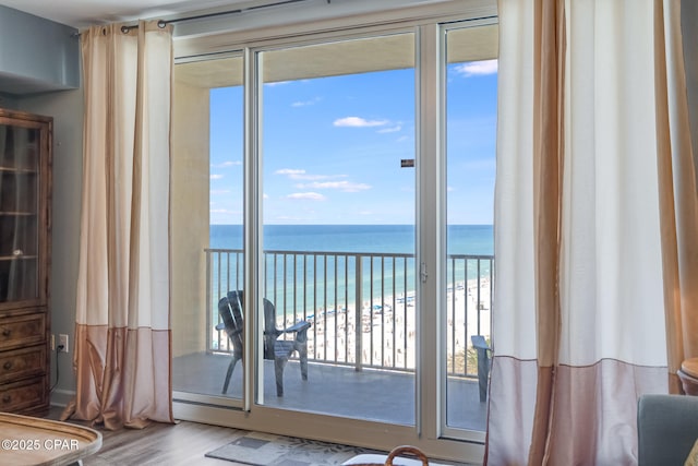 doorway to outside with a water view, wood finished floors, and a view of the beach
