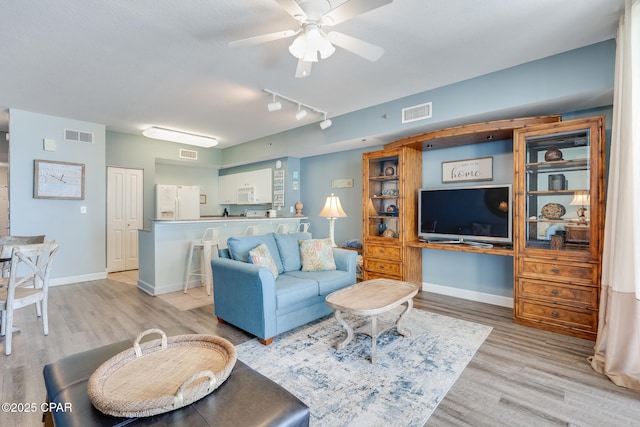 living area featuring visible vents, baseboards, light wood-style floors, and ceiling fan