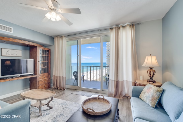living area with wood finished floors, baseboards, visible vents, a water view, and ceiling fan