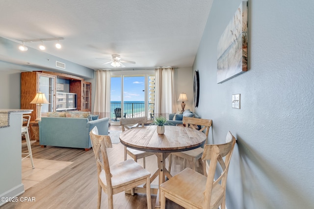 dining space featuring a water view, a textured ceiling, light wood finished floors, visible vents, and a ceiling fan