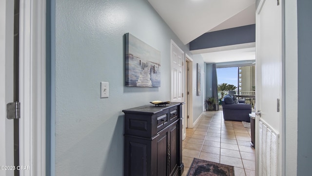 corridor featuring baseboards, lofted ceiling, visible vents, and light tile patterned floors