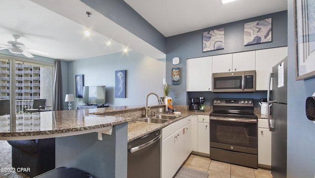 kitchen with white cabinets, a peninsula, ceiling fan, stainless steel appliances, and a sink