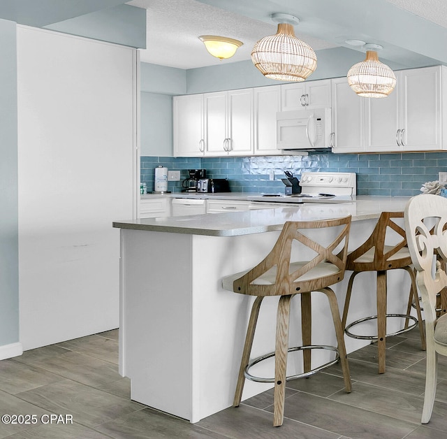 5801 Thomas Dr Unit 1216, Panama City Beach, FL 32408 - kitchen featuring tasteful backsplash, white appliances, a breakfast bar, white cabinetry, and a peninsula