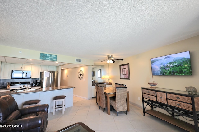 living area with a textured ceiling, light tile patterned floors, ceiling fan, and baseboards