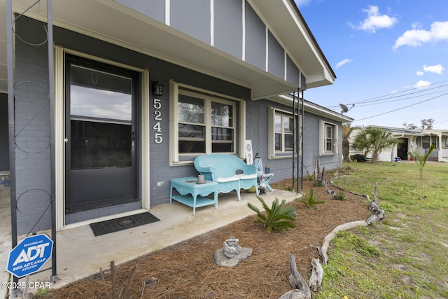 doorway to property featuring a lawn, covered porch, and brick siding