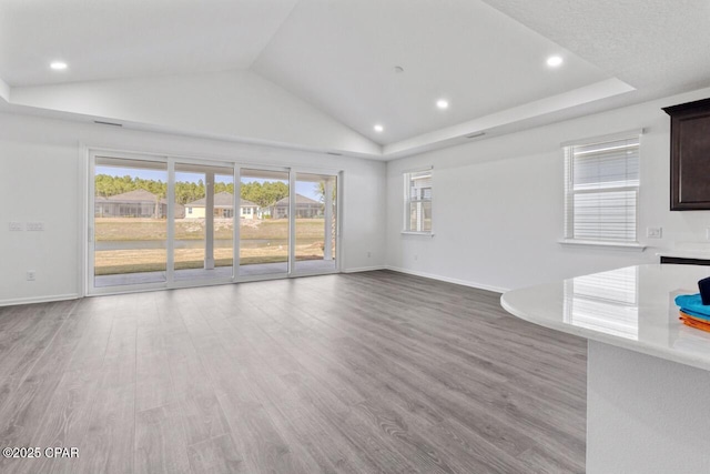 unfurnished living room featuring a healthy amount of sunlight, wood finished floors, baseboards, and vaulted ceiling