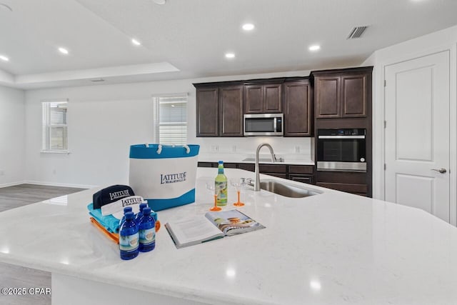 kitchen featuring dark brown cabinetry, wood finished floors, a sink, stainless steel appliances, and a center island with sink