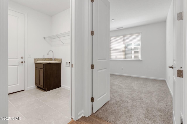 laundry room featuring light colored carpet, baseboards, a sink, and visible vents