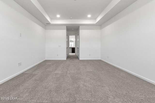 empty room with a tray ceiling, carpet flooring, baseboards, and recessed lighting