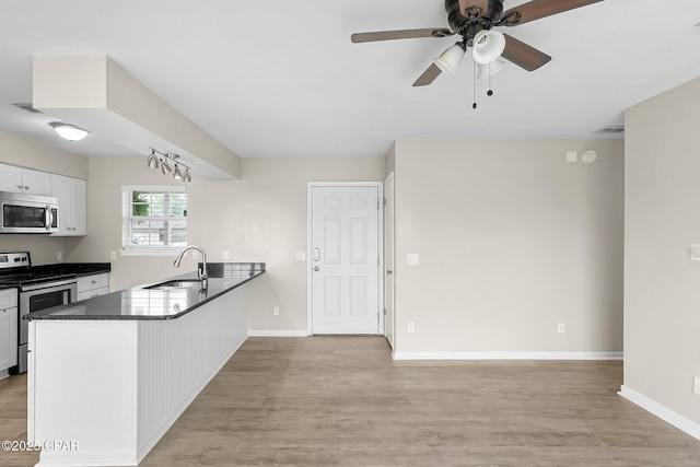 kitchen with a sink, a peninsula, light wood-type flooring, stainless steel appliances, and dark countertops
